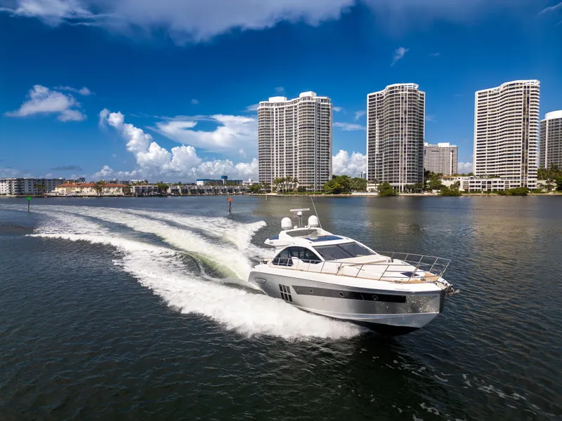 Slide: The Image of 2016 Azimut 55S yacht cruising near modern high-rise buildings under a clear blue sky. - 2