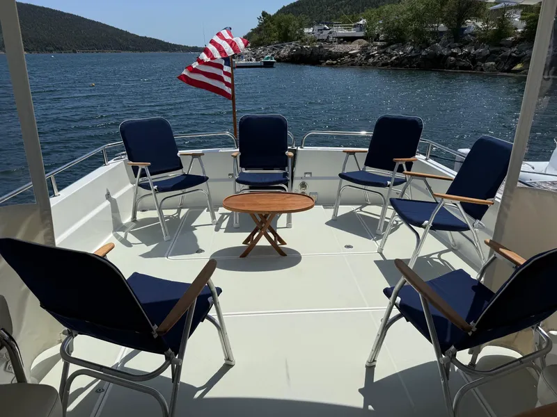 Slide: The Image of 2019 Back Cove Downeast boat deck with chairs, table, and American flag, overlooking scenic water. - 15