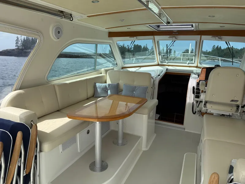 Slide: The Image of 2019 Back Cove Downeast boat interior with beige seating, wooden table, and scenic water view. - 30