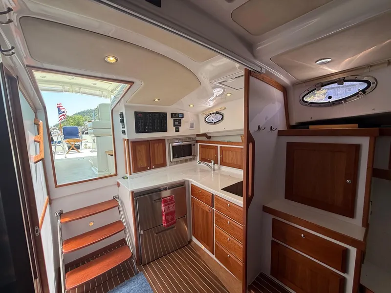 Slide: The Image of 2019 Back Cove Downeast yacht interior with wooden cabinetry, kitchenette, and outdoor view. - 36