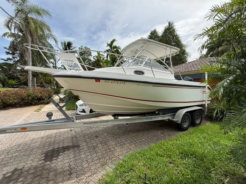 The Image of 1998 Boston Whaler 23 Conquest boat on trailer, parked in a driveway, surrounded by palm trees. - 0