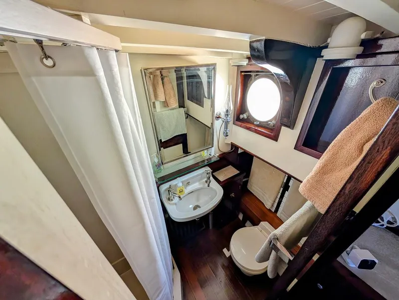 Slide: The Image of 1936 Classic Motorsailer bathroom with porthole, shower, sink, and wooden accents. - 32