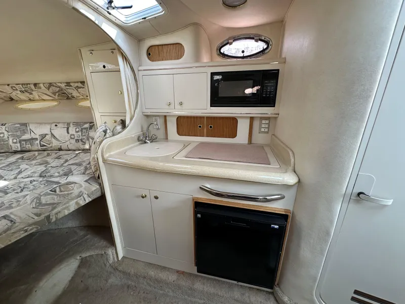 Slide: The Image of 1998 Sea Ray 290 Sundancer interior with kitchenette, featuring microwave, sink, and compact fridge. - 19