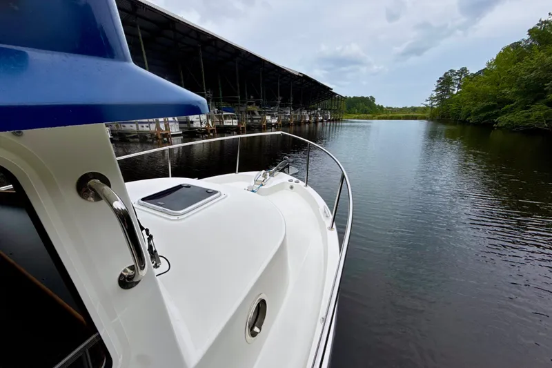 Slide: The Image of 2023 Nordic Tug 34 Tug on calm water near marina and trees. - 10
