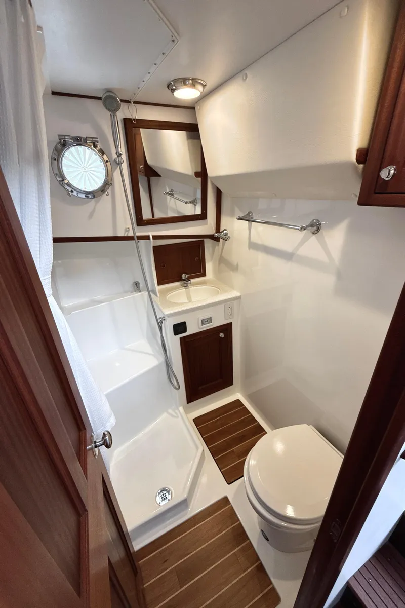 Slide: The Image of 2023 Nordic Tug 34 Tug bathroom with shower, sink, and toilet, featuring wood accents and porthole. - 25