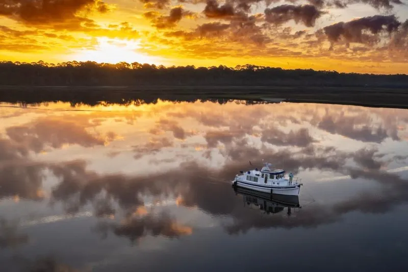 Slide: The Image of 2023 Nordic Tug 34 on tranquil water at sunset, reflecting vibrant sky. - 29