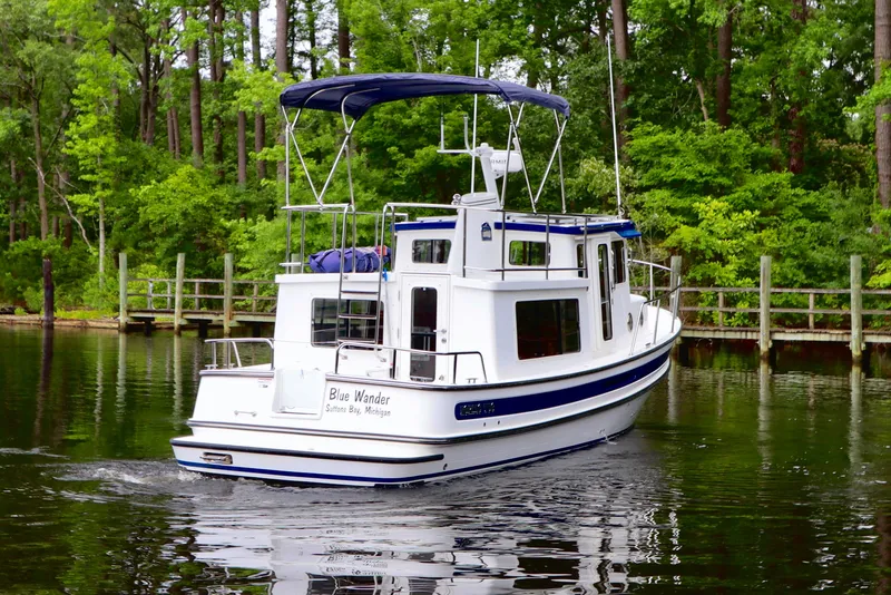 Slide: The Image of 2023 Nordic Tug 34 cruising on a serene, tree-lined waterway. - 3