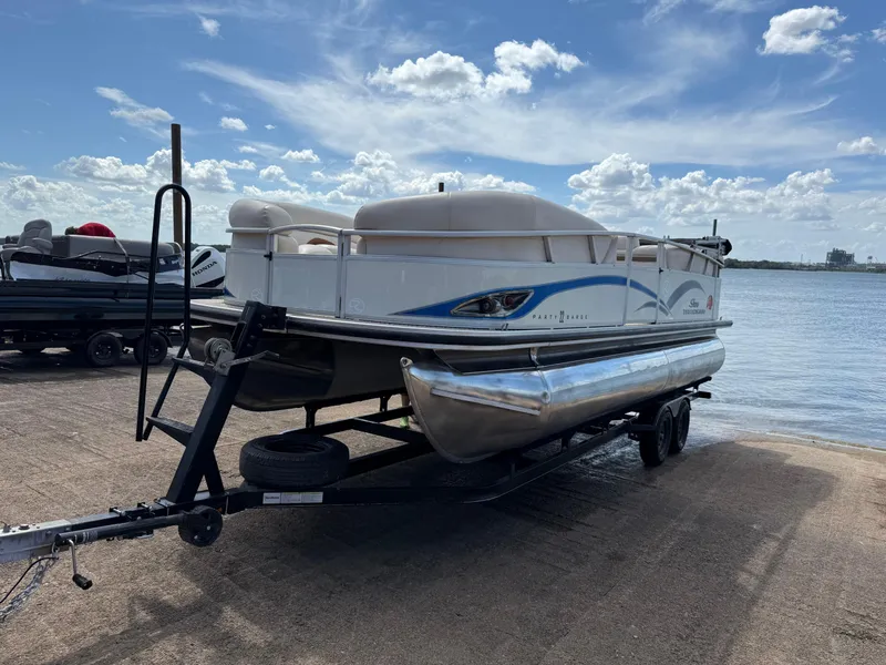 The Image of 2011 Sun Tracker Regency Party Barge 22 on trailer by a lake under blue sky. - 0