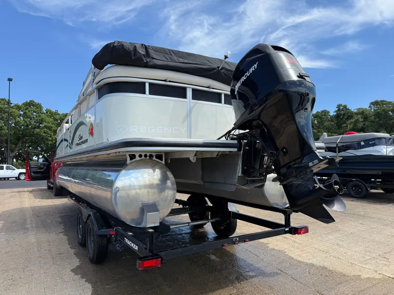 Slide: The Image of 2011 Sun Tracker Regency Party Barge 22 on trailer, parked near water, under clear sky. - 10