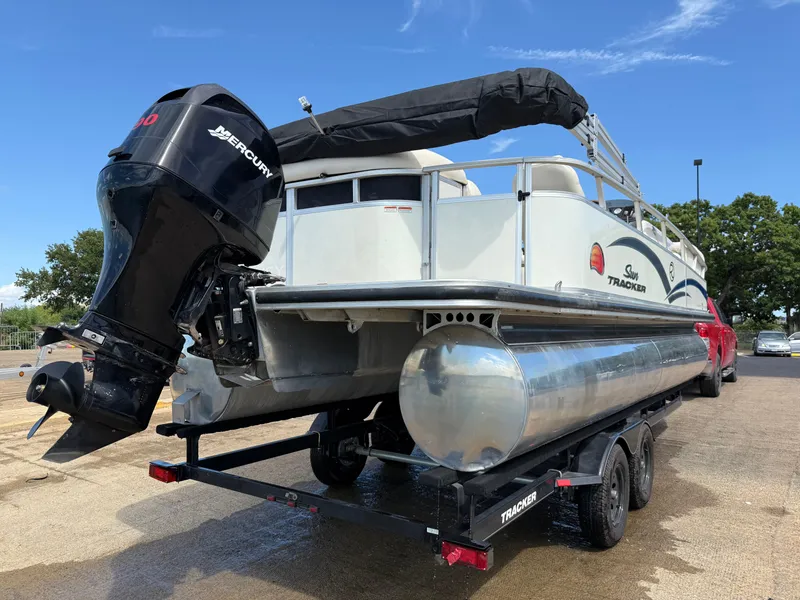 Slide: The Image of 2011 Sun Tracker Regency Party Barge 22 on trailer by the water under a blue sky. - 13