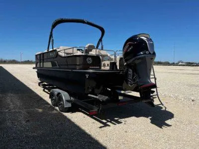 Slide: The Image of 2025 SunCatcher Elite 324 SS pontoon boat on trailer, parked on gravel under clear blue sky. - 5
