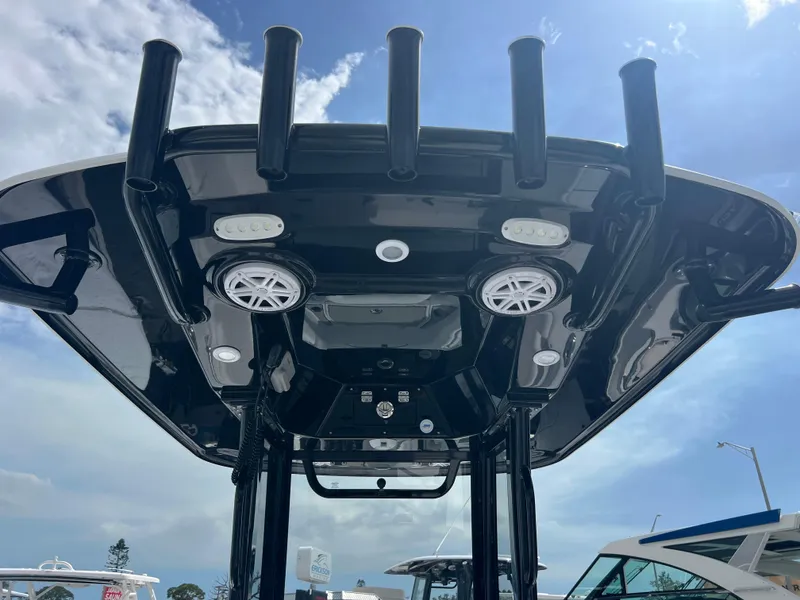 Slide: The Image of 2025 Sportsman Masters 247OE Bay Boat T-top with rod holders and speakers under blue sky. - 22