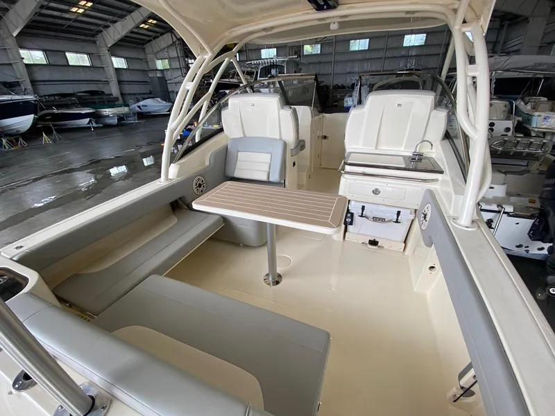 Slide: The Image of 2026 Scout 255 Dorado boat interior with seating, table, and kitchenette in a showroom. - 5