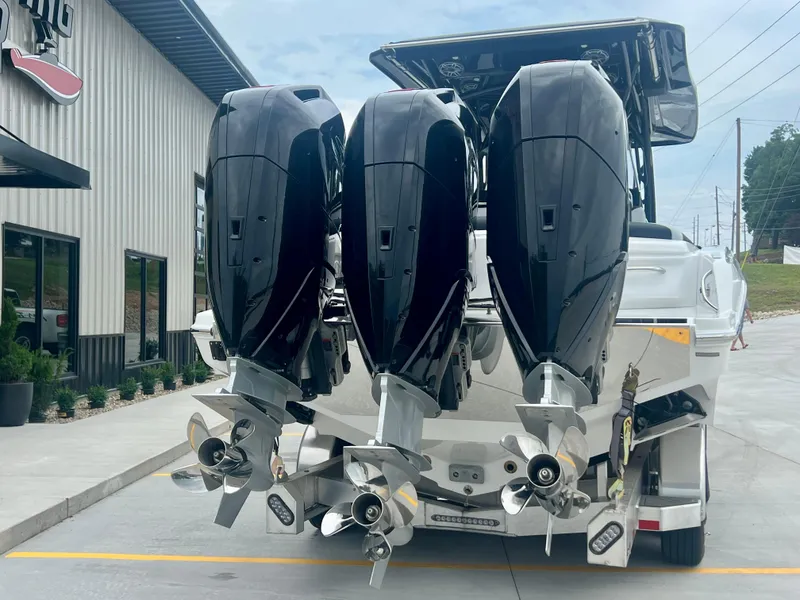 Slide: The Image of 2025 Nor-Tech 340 Sport Center Console with triple outboard engines, parked outside a building. - 46