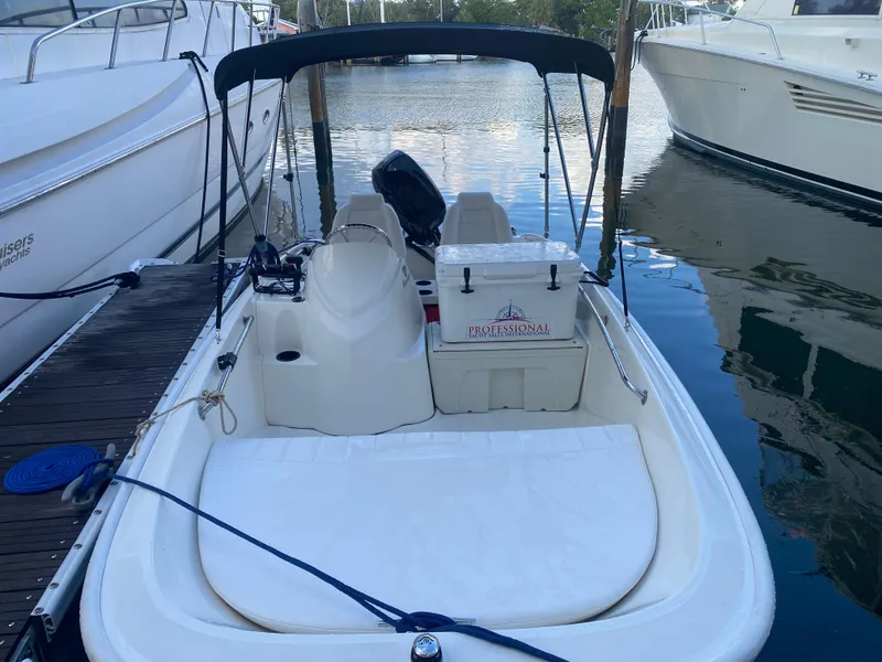 Slide: The Image of 2018 Boston Whaler 150 Super Sport docked between boats, featuring a canopy and seating area. - 13