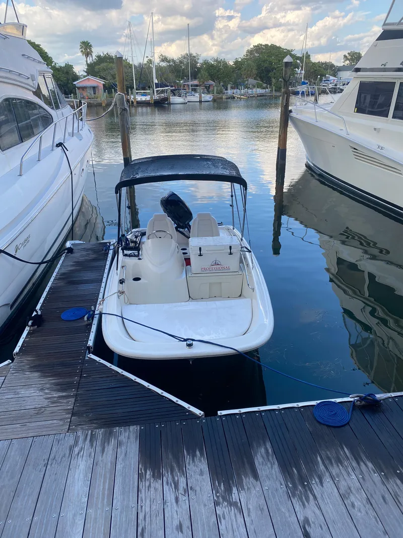 Slide: The Image of 2018 Boston Whaler 150 Super Sport docked between larger boats in a marina. - 14