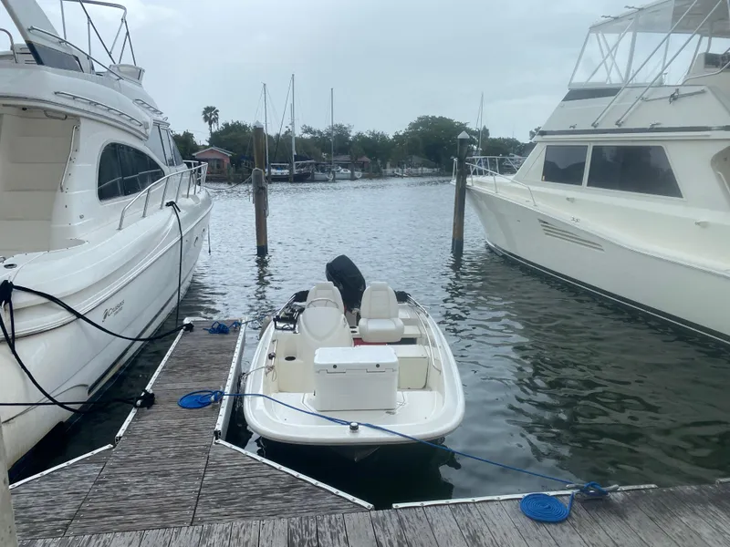 Slide: The Image of 2018 Boston Whaler 150 Super Sport docked between larger boats in a marina. - 15