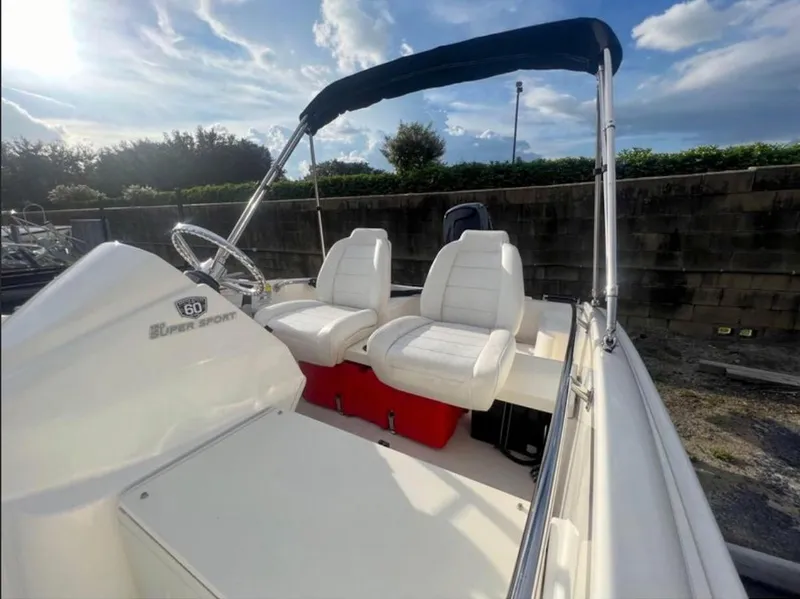 Slide: The Image of 2018 Boston Whaler 150 Super Sport boat with white seats and canopy under a blue sky. - 2