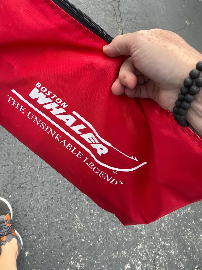 Slide: The Image of Red Boston Whaler bag with "The Unsinkable Legend" logo, held by a person. - 23