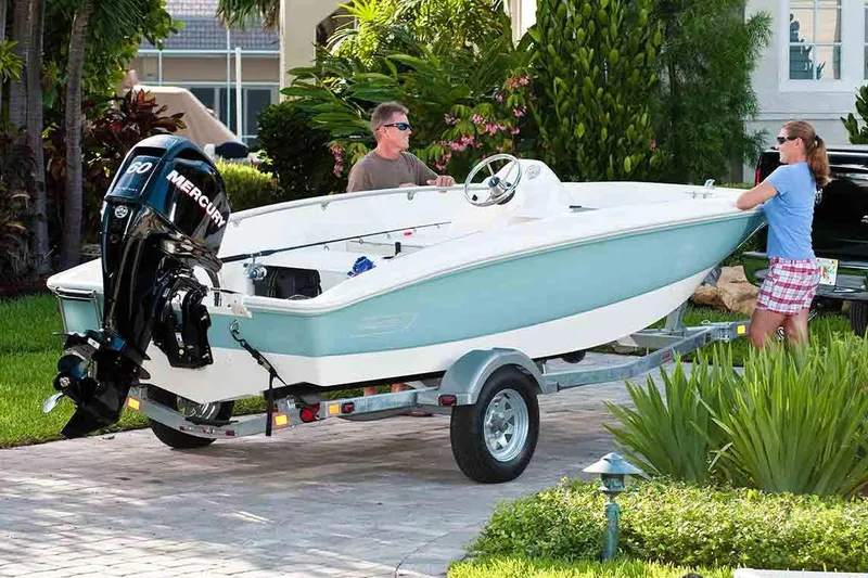 Slide: The Image of 2018 Boston Whaler 150 Super Sport on trailer, parked in a driveway with two people nearby. - 29