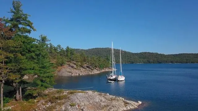 Slide: The Image of Sailboats anchored in a serene bay, surrounded by lush greenery and rocky shores. - 15