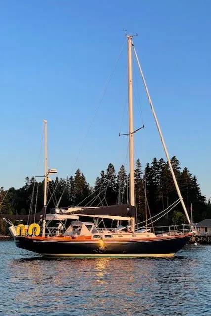 Slide: The Image of 1967 Hinckley Bermuda 40 sailboat on calm water at sunset, with forested shoreline. - 18