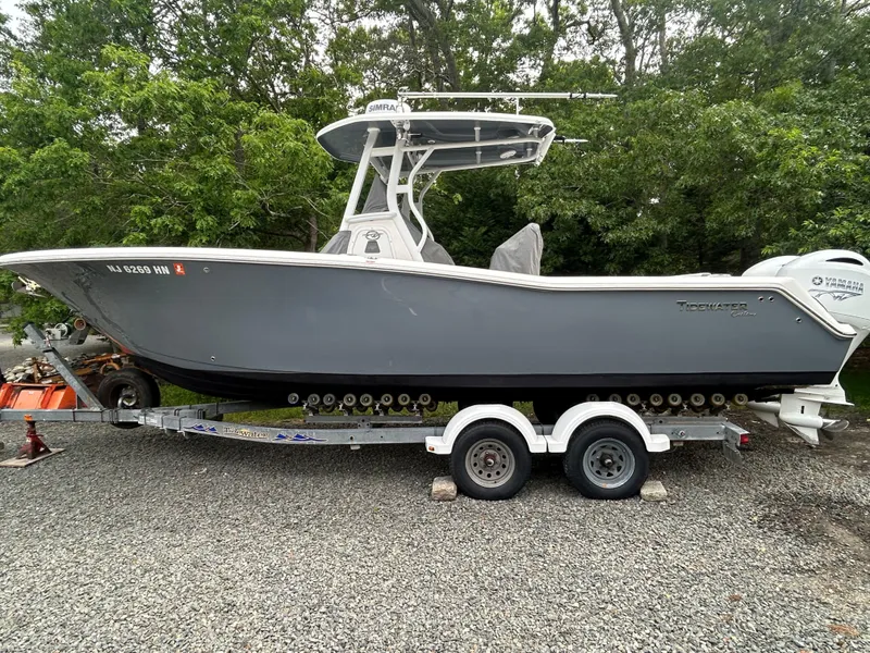 The Image of 2020 Tidewater 272 CC Adventure boat on trailer, parked on gravel with trees in background. - 1