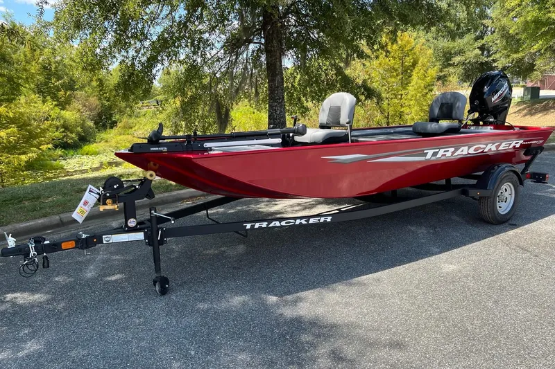The Image of 2025 Tracker Panfish 17 boat in red, parked on a trailer, surrounded by greenery. - 2