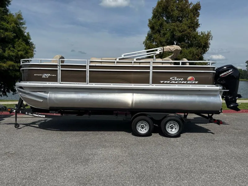 The Image of 2025 Sun Tracker SportFish 20 DLX pontoon boat on trailer, parked near a lake. - 0