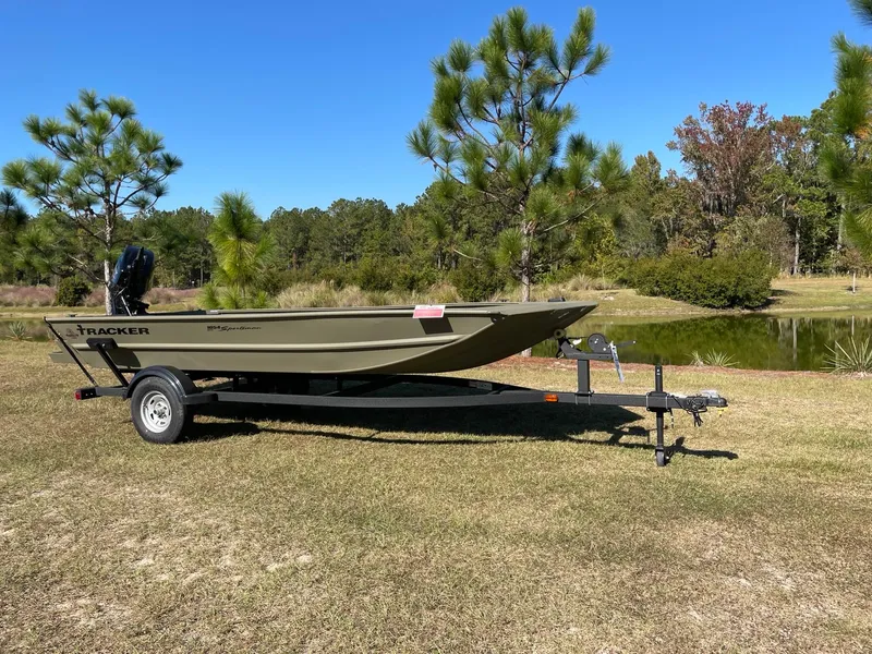 The Image of 2025 Tracker Grizzly 1654 T Sportsman boat on trailer, parked on grassy area near pond. - 0