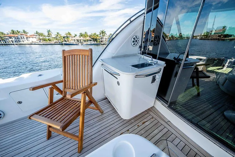 Slide: The Image of 2012 Sea Ray 610 Sundancer yacht deck with wooden chair and sink, overlooking water. - 14