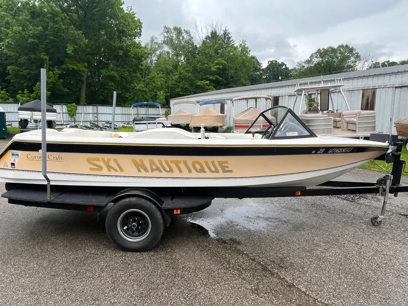 The Image of 1990 Correct Craft Ski Nautique boat on trailer, parked outdoors near trees and buildings. - 1
