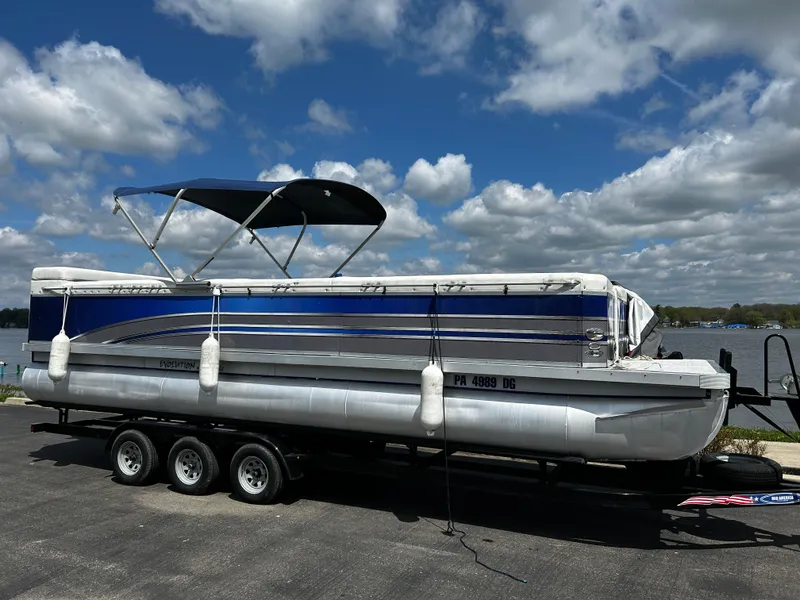 The Image of 2005 Evolution 26 pontoon boat on trailer under a blue sky. - 1