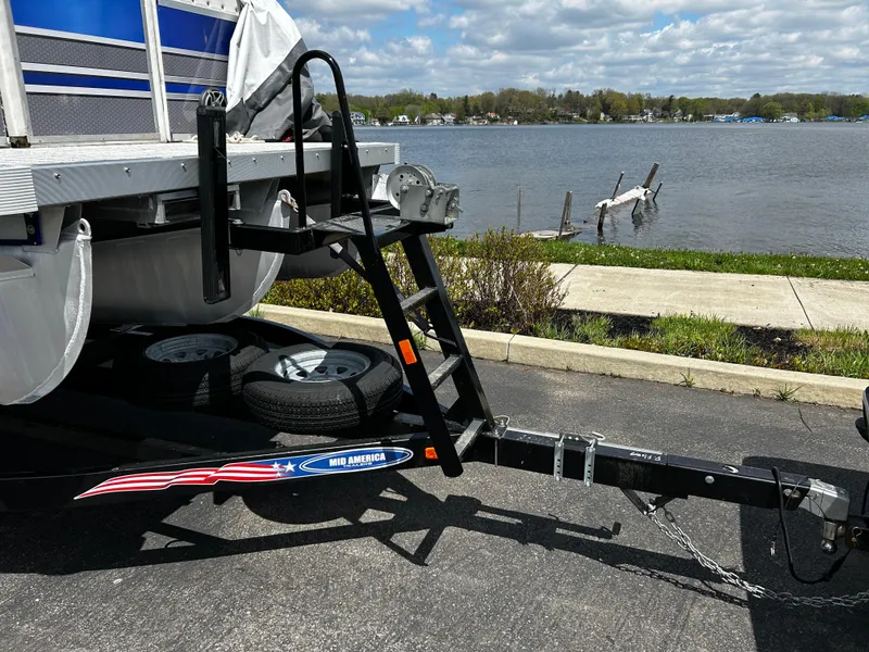 Slide: The Image of Trailer hitch and ladder of a 2005 Evolution 26 boat by a lakeside. - 2