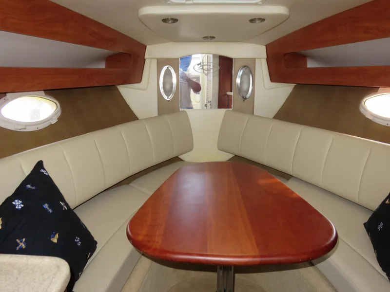 Slide: The Image of 2008 Rinker 280 Express Cruiser cabin with wood table and beige seating. - 10