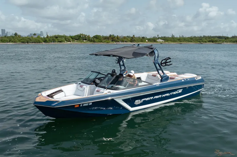 Slide: The Image of 2019 Nautique Super Air Nautique GS24 boat on calm water, with lush shoreline in background. - 16