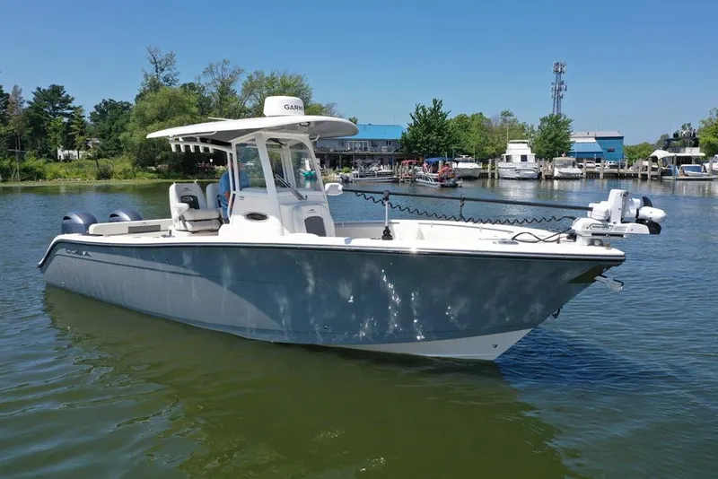 Slide: The Image of 2023 Cobia 280 Center Console boat on calm water, surrounded by greenery and docks. - 33