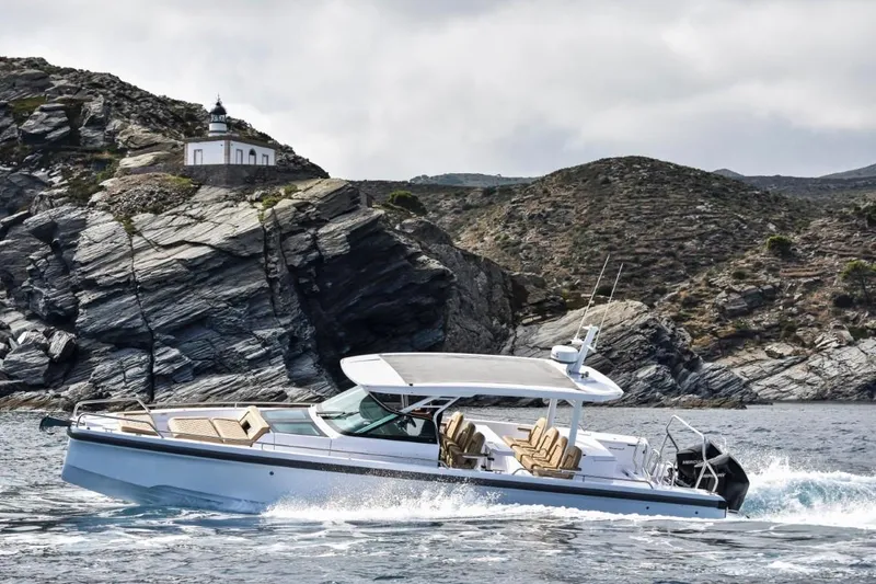 Slide: The Image of 2025 Axopar 37 Sun Top cruising near rocky coastline with lighthouse in background. - 15