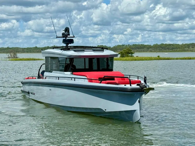 Slide: The Image of 2023 Axopar Shadow 900XC boat cruising on a scenic lake under a cloudy sky. - 2