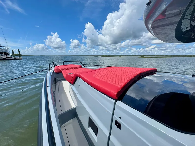 Slide: The Image of 2023 Axopar Shadow 900XC boat with red seating, on a calm lake under a blue sky. - 5