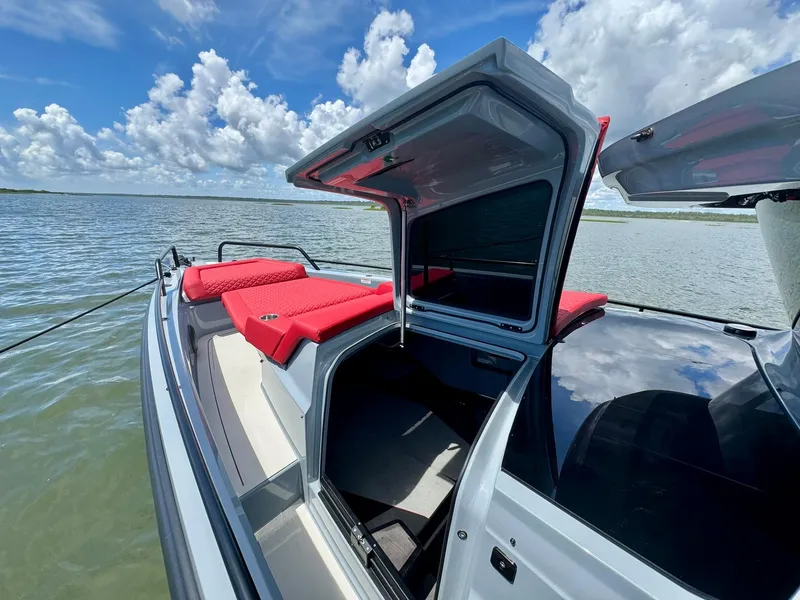 Slide: The Image of 2023 Axopar Shadow 900XC boat with open deck, red seating, and scenic water view. - 6