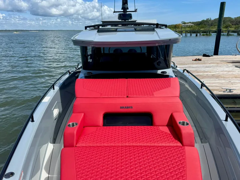 Slide: The Image of 2023 Axopar Shadow 900XC with vibrant red seating, docked by a serene waterfront. - 7