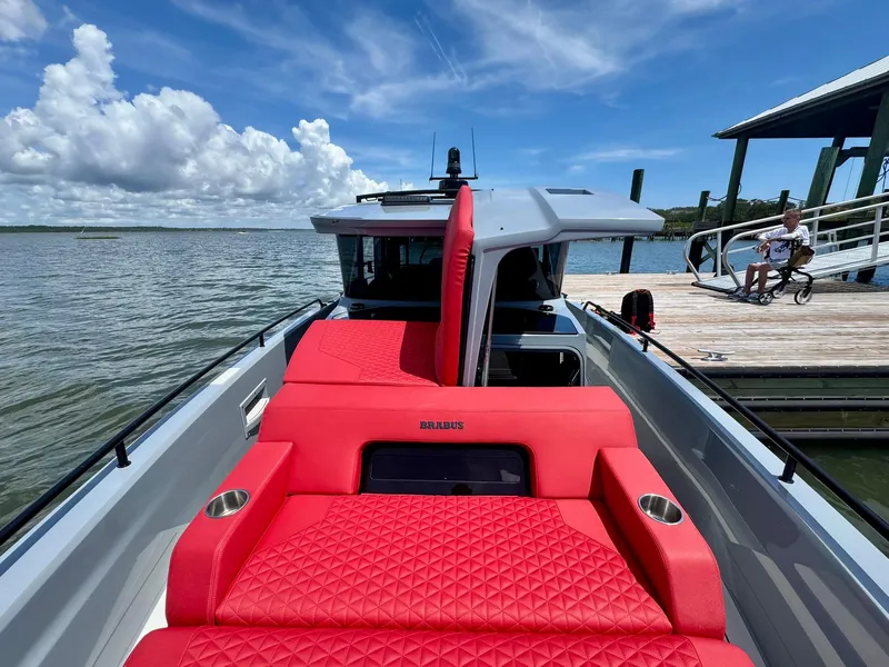 Slide: The Image of 2023 Axopar Shadow 900XC with red seating, docked by a scenic waterfront. - 8