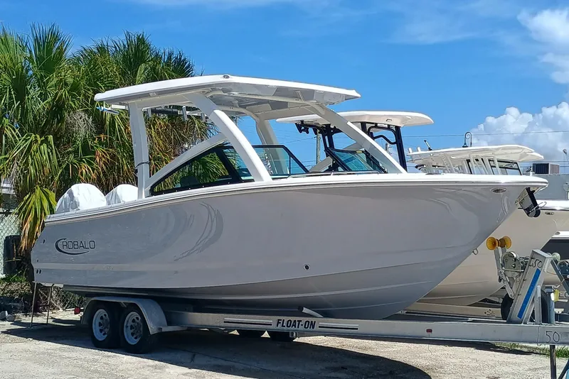 Slide: The Image of 2025 Robalo R257 Dual Console boat on trailer, parked near palm trees under blue sky. - 1