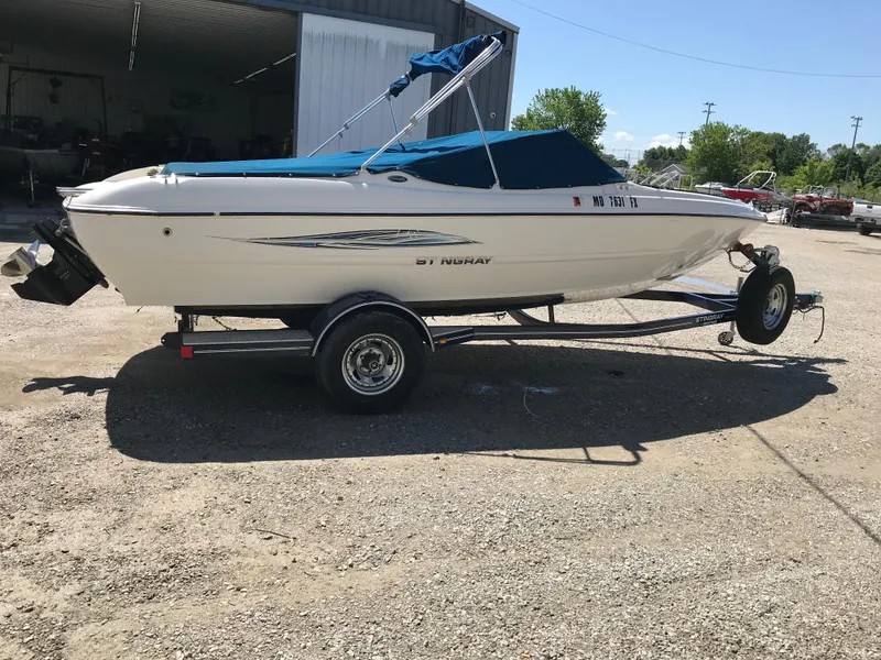 The Image of 2012 Stingray 195 RX boat on trailer, parked outdoors, with blue canopy. - 1