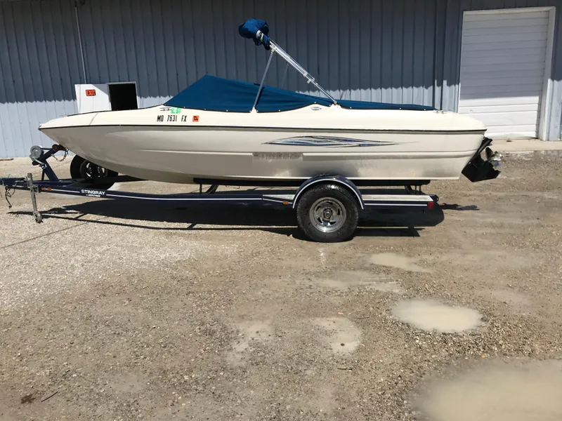 Slide: The Image of 2012 Stingray 195 RX boat on trailer, parked outdoors with blue cover. - 2