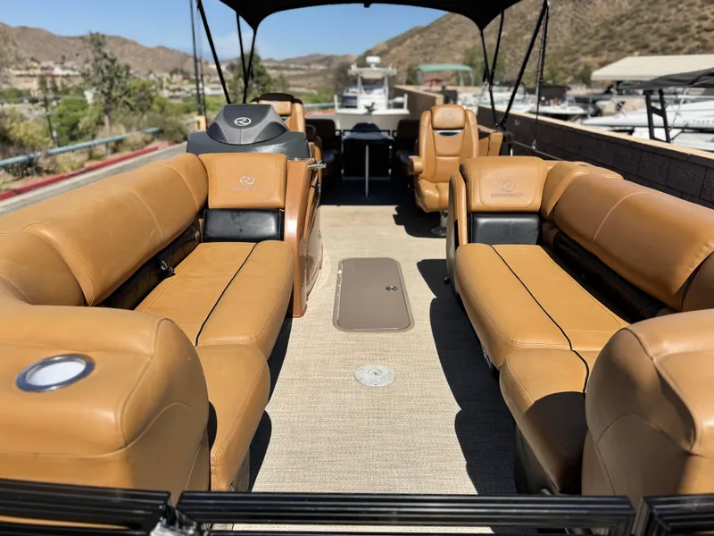 Slide: The Image of 2021 Regency 230 LE3 pontoon boat with tan leather seating and canopy, docked in a scenic area. - 10