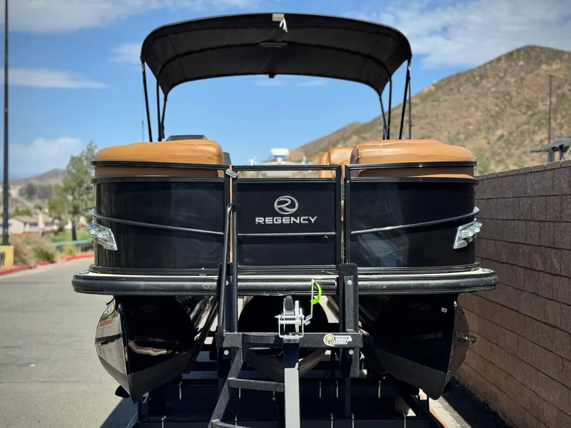 Slide: The Image of 2021 Regency 230 LE3 pontoon boat on trailer, parked outdoors with scenic mountain backdrop. - 2
