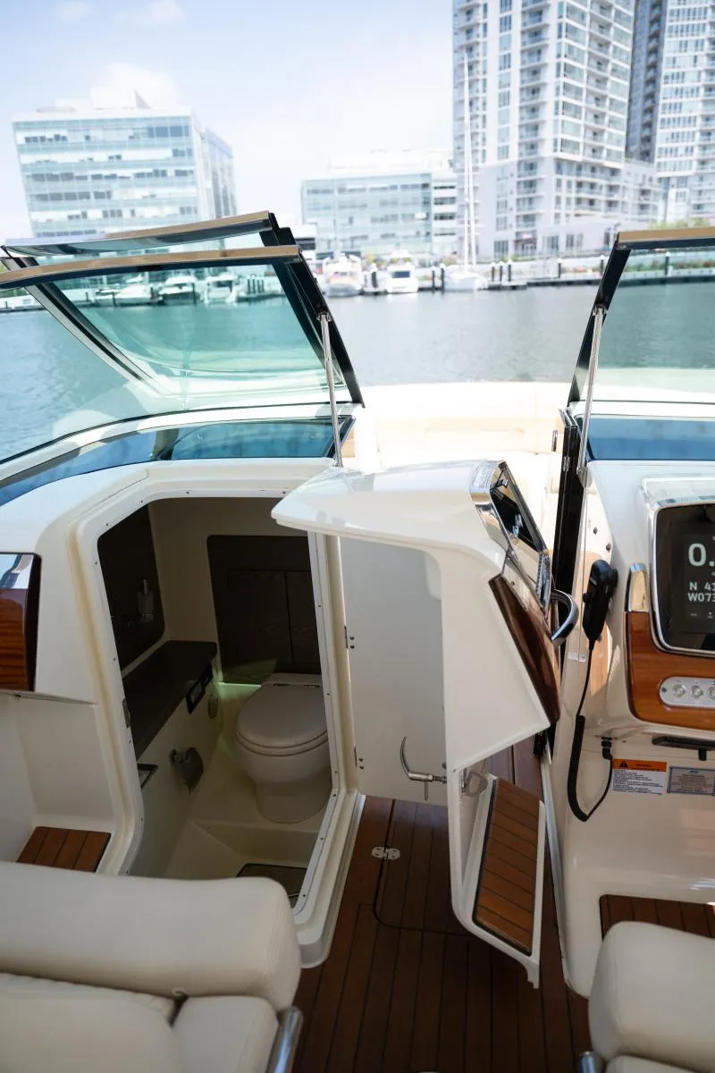 Slide: The Image of 2021 Chris-Craft Launch GT boat interior with open cabin door, docked near modern buildings. - 27