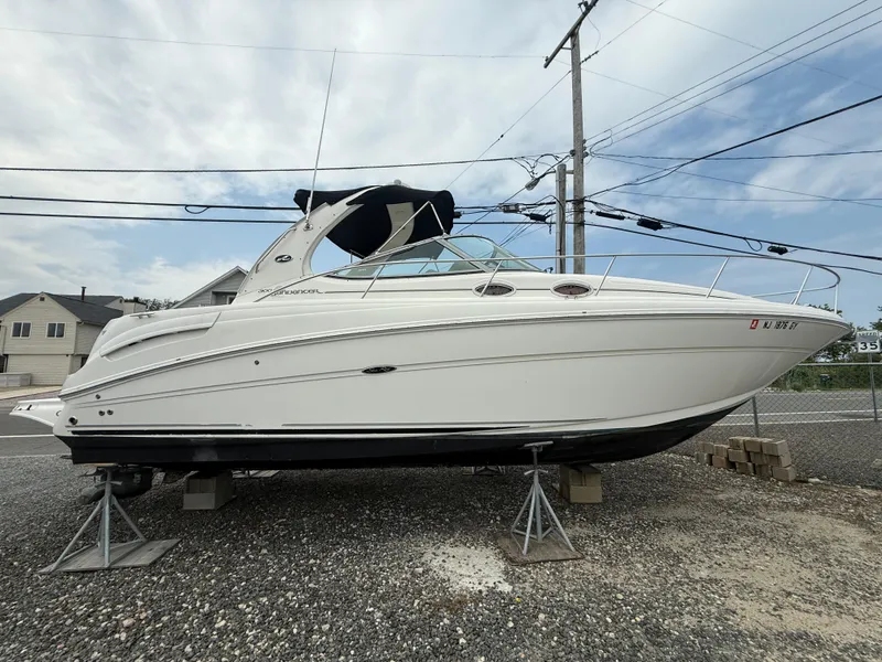 The Image of 2006 Sea Ray 300 Sundancer boat on stands, displayed outdoors under cloudy sky. - 1